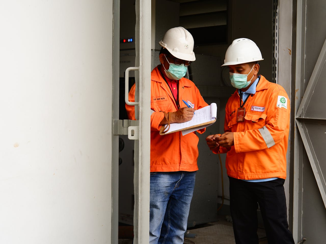 Two construction workers in safety gear discussing plans at a site entrance.