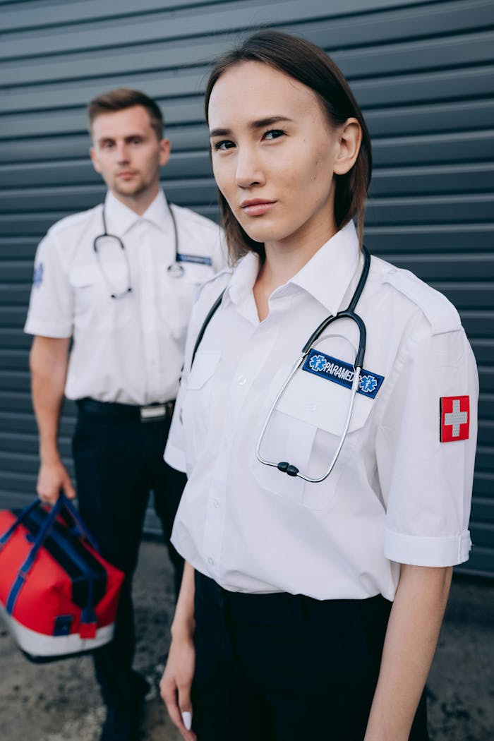 Two paramedics in white uniform shirts standing with medical equipment. Ready for action.