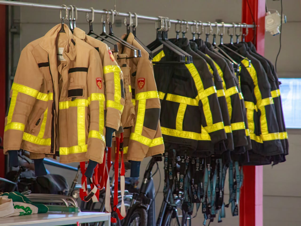 Firefighter uniforms with reflective strips hanging in a garage setting.