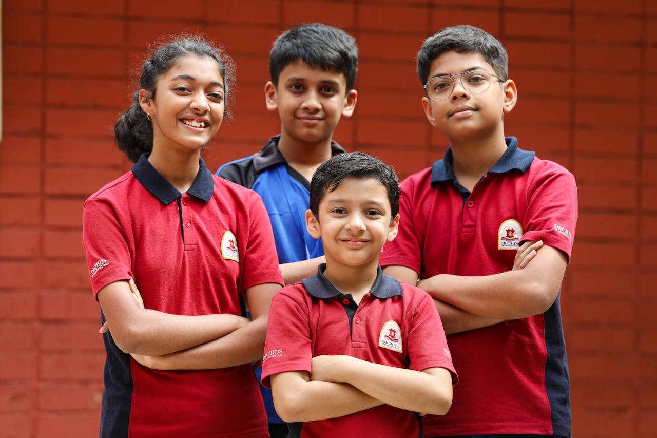 A group of diverse schoolchildren smiling confidently with arms crossed, standing against a brick wall.