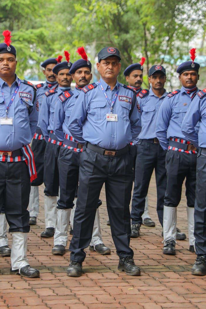 A group of Indian security guards in uniform standing outdoors with red plume caps, exuding discipline.
