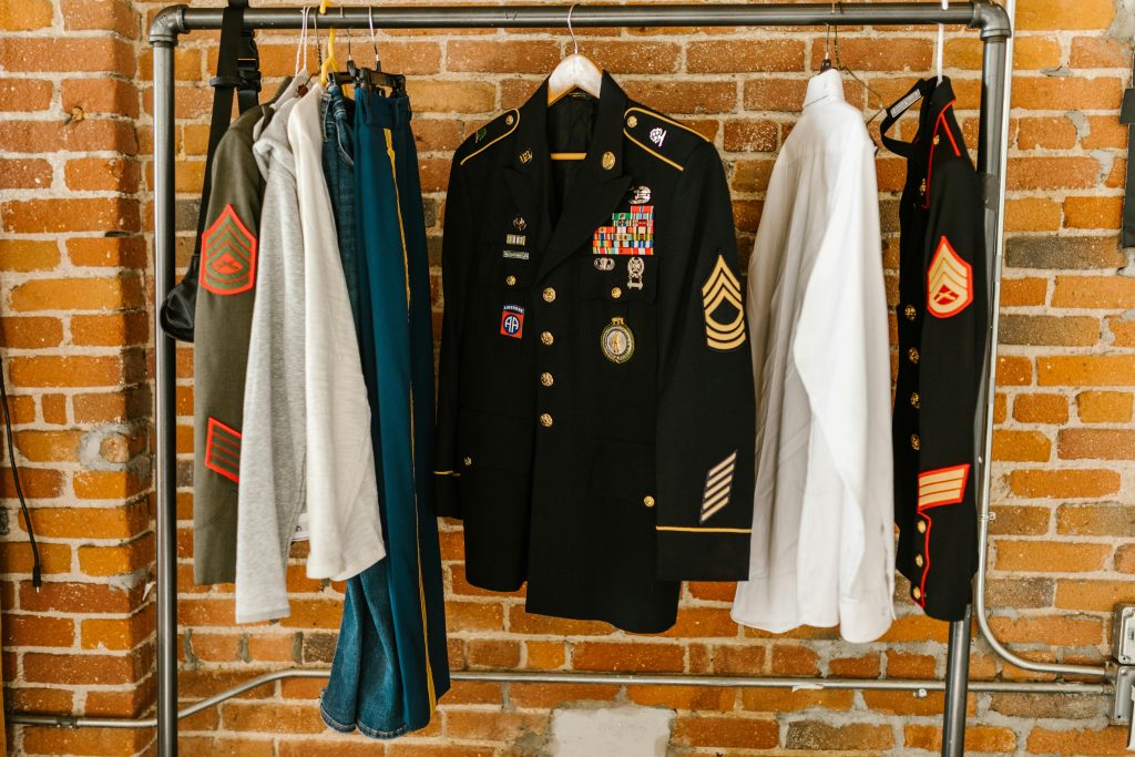 Military uniforms with badges hanging against a brick wall background.